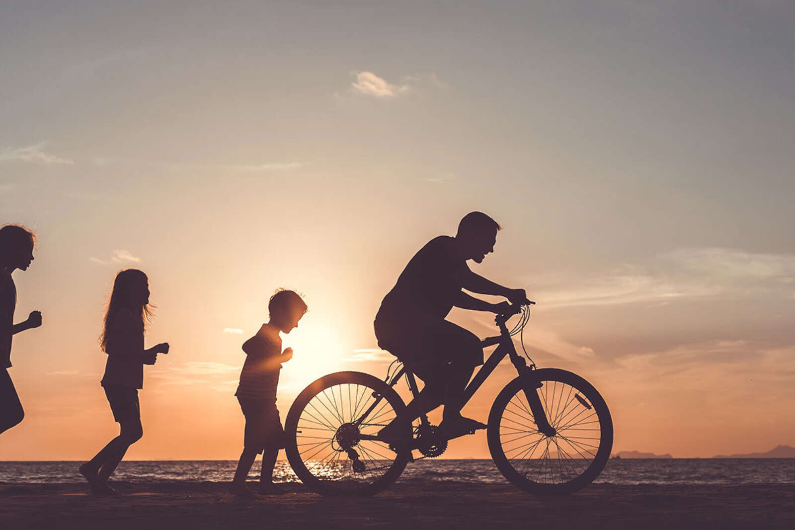 Children following a man riding a bike at sunset